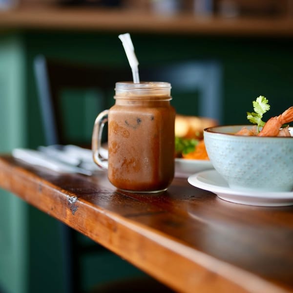 Iced Thai tea in a mason jar with a straw, next to a bowl of shrimp soup.
