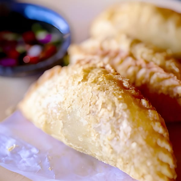 Close-up of golden-brown Thai curry puffs with a small bowl of dipping sauce in the background.