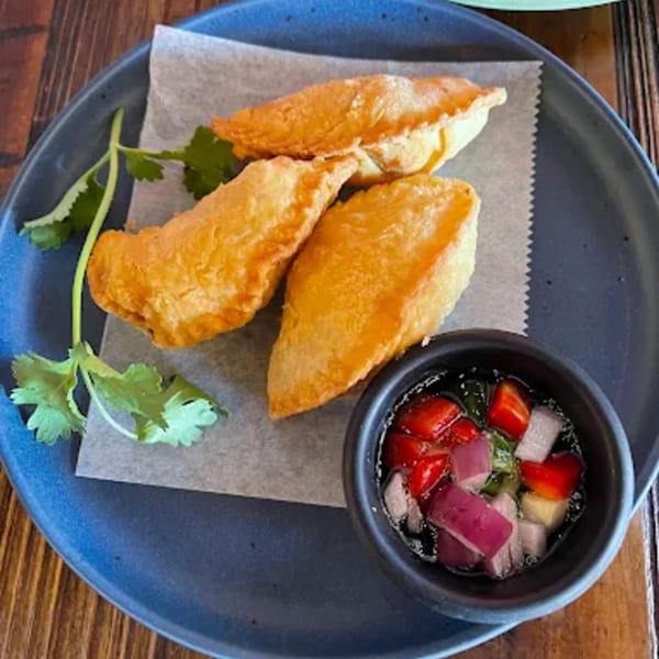 Three crispy Thai curry puffs with cilantro and a dipping sauce on a blue plate.